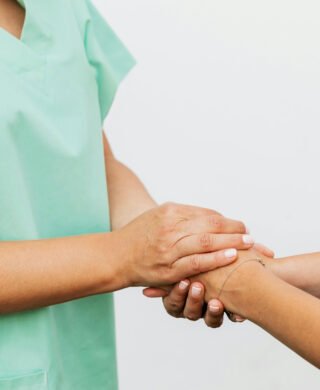 A medical provider in scrubs holds hands with a person who is out of frame, used to explain the symptoms of uterine fibroids