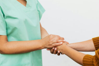 A medical provider in scrubs holds hands with a person who is out of frame, used to explain the symptoms of uterine fibroids