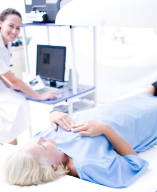 A photograph of a woman undergoing a DEXA bone density scan while a technologist operates an imaging machine