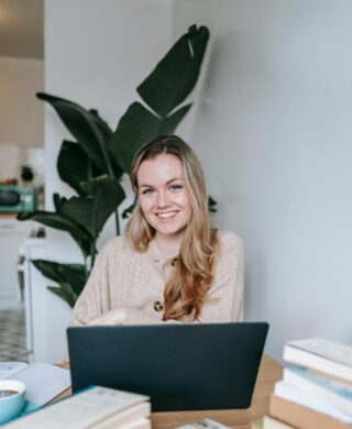 A young blond haired woman sitting in front of a laptop and smiling
