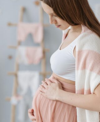 A pregnant woman holds her belly while looking down, used to explain mammogram guidelines during pregnancy